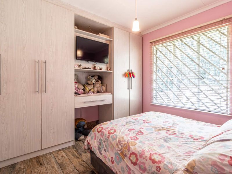 A well-maintained bedroom featuring light wood-grain built-in wardrobes, laminate flooring, and venetian blinds, offering a functional and tidy living space.