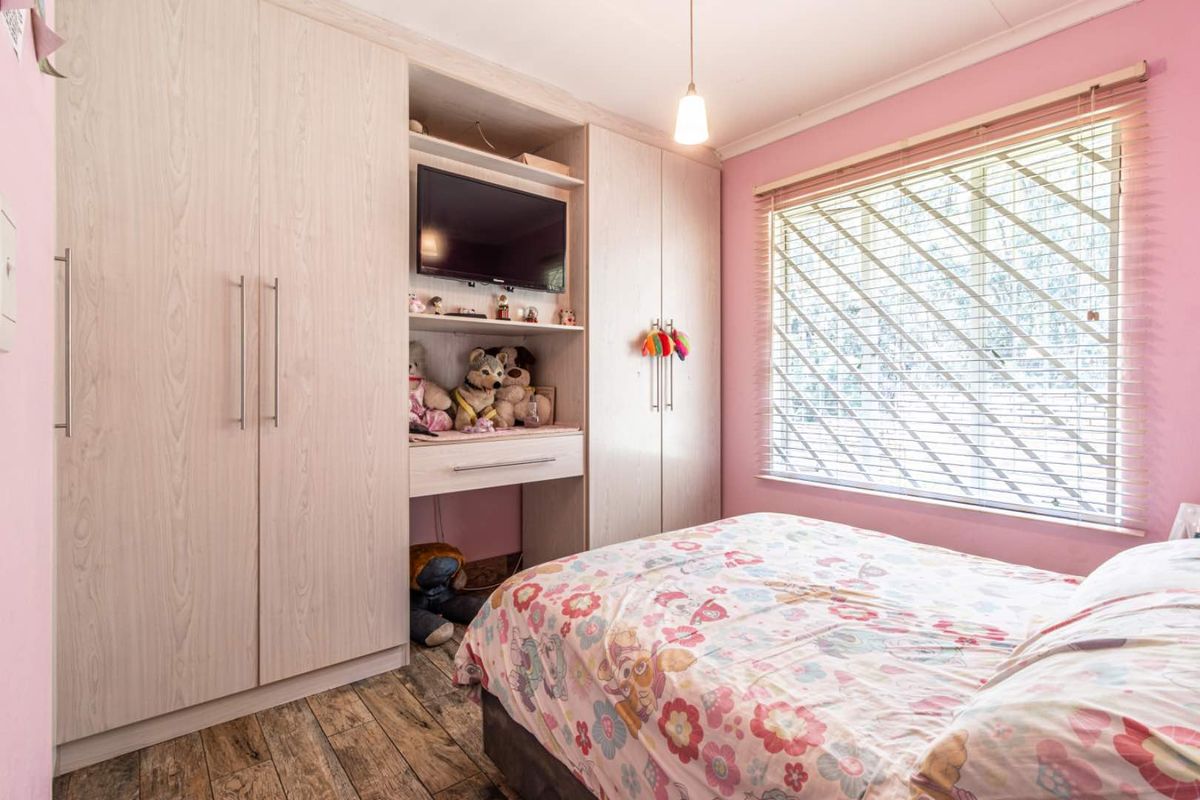 A well-maintained bedroom featuring light wood-grain built-in wardrobes, laminate flooring, and venetian blinds, offering a functional and tidy living space.
