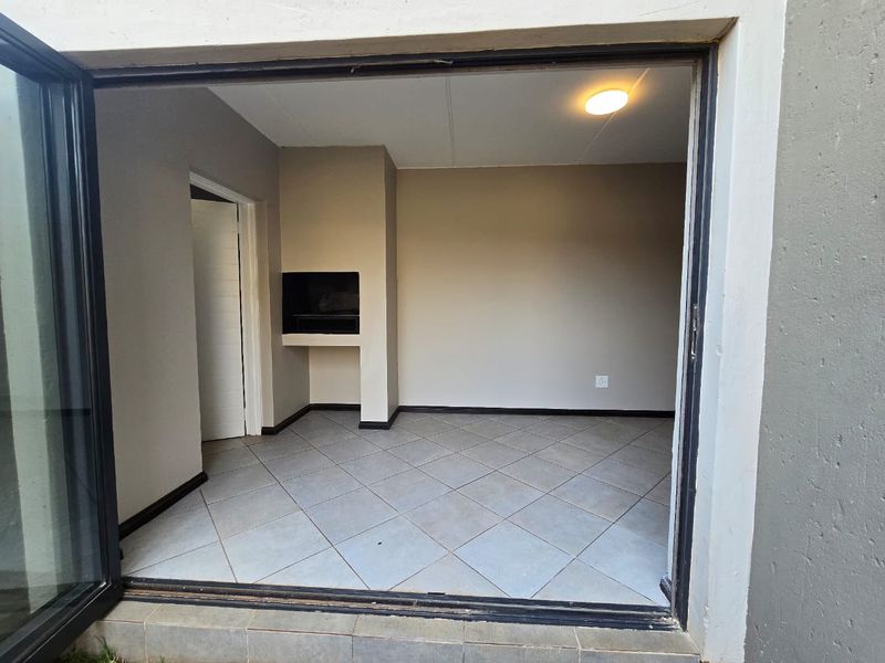 An empty living area featuring tiled flooring and a built-in braai, accessible via a large sliding door.