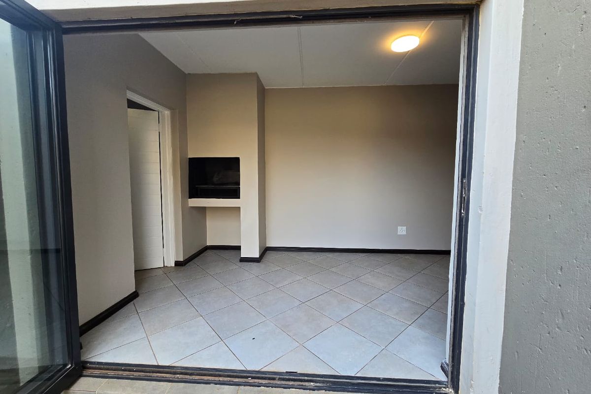 An empty living area featuring tiled flooring and a built-in braai, accessible via a large sliding door.