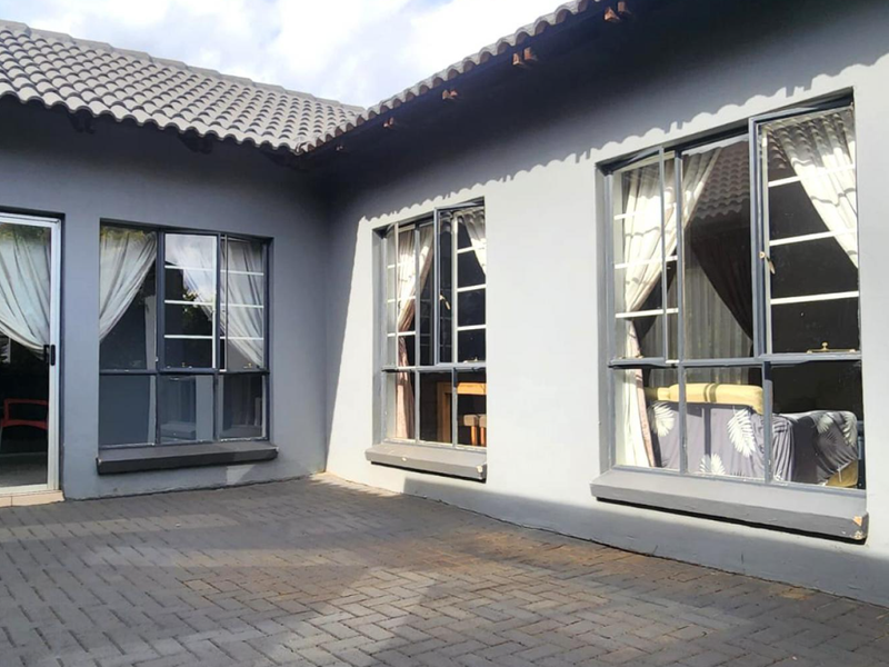 A paved rear patio area featuring grey exterior walls, aluminium-framed windows, and a sliding glass door leading into the home.