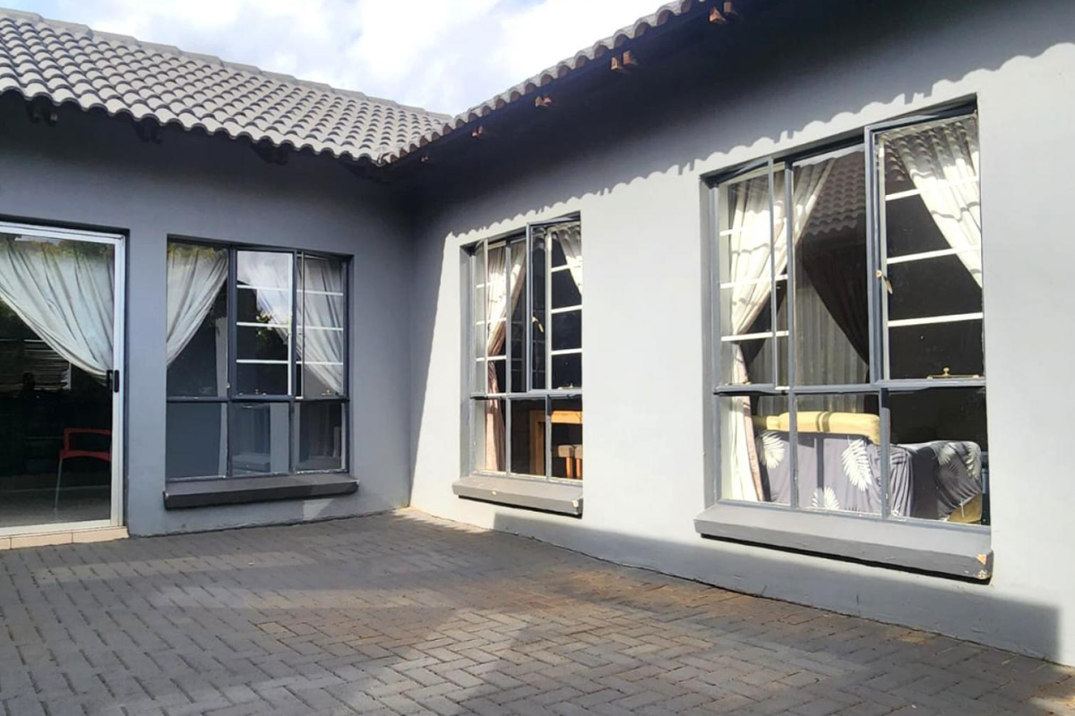 A paved rear patio area featuring grey exterior walls, aluminium-framed windows, and a sliding glass door leading into the home.