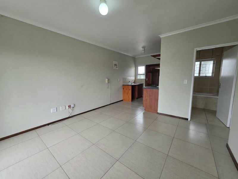 An open-plan living area featuring tiled flooring, neutral walls, and a compact kitchen corner, with an adjacent bathroom entrance.