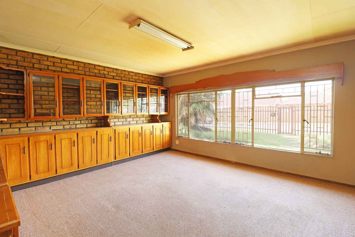 Spacious living area featuring extensive built-in wooden cabinetry, exposed brick accents, and large windows with security bars, offering a bright and functional space.
