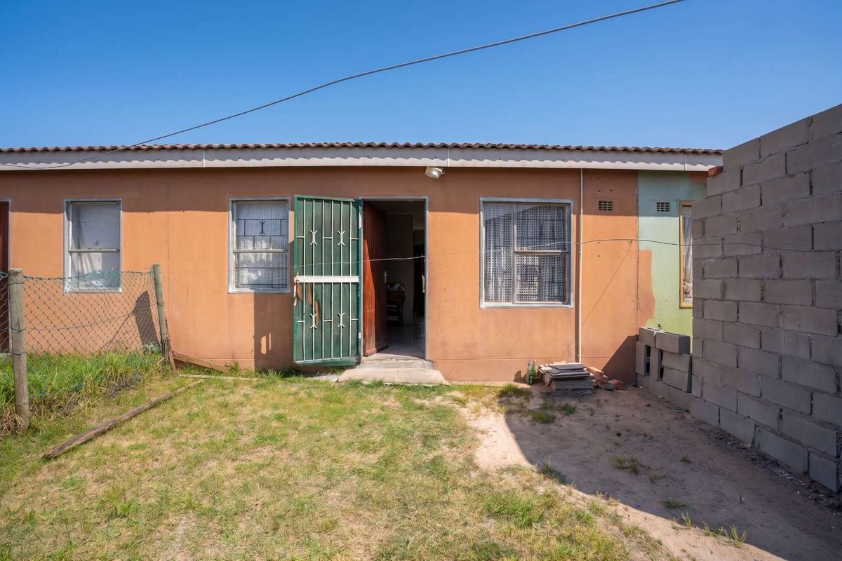Rear view of the property featuring a simple facade, security gate, and a small backyard area with a concrete block boundary wall.