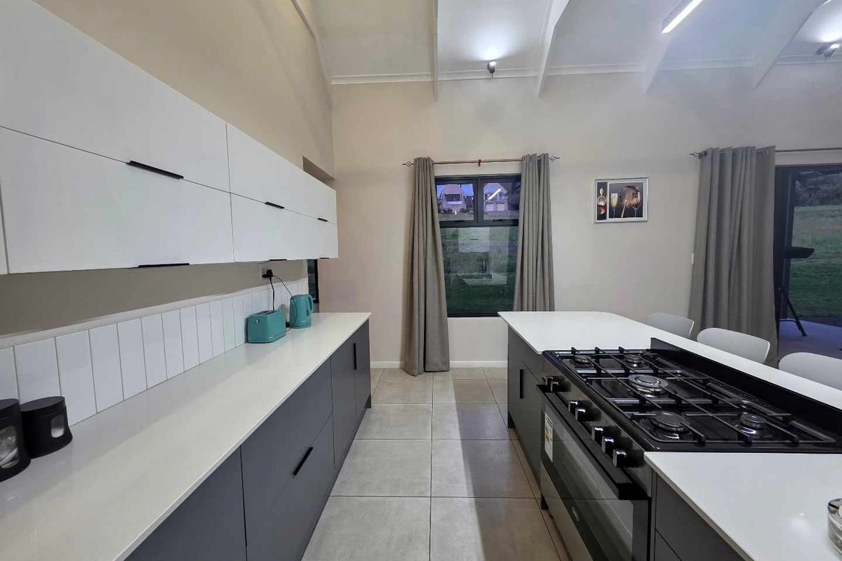 Modern kitchen featuring sleek grey cabinetry, white countertops, a central island with a built-in gas hob, and high vaulted ceilings.