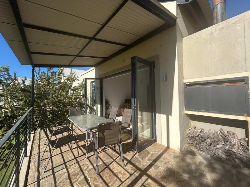 A covered patio featuring stone flooring, a built-in braai, and folding glass doors that provide seamless access to the interior living space.