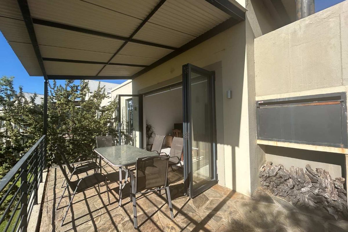 A covered patio featuring stone flooring, a built-in braai, and folding glass doors that provide seamless access to the interior living space.