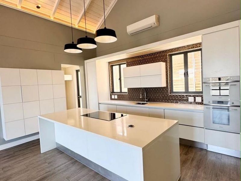 Modern, spacious kitchen featuring a large central island, high-end built-in appliances, sleek cabinetry, and a striking vaulted ceiling with exposed timber beams.