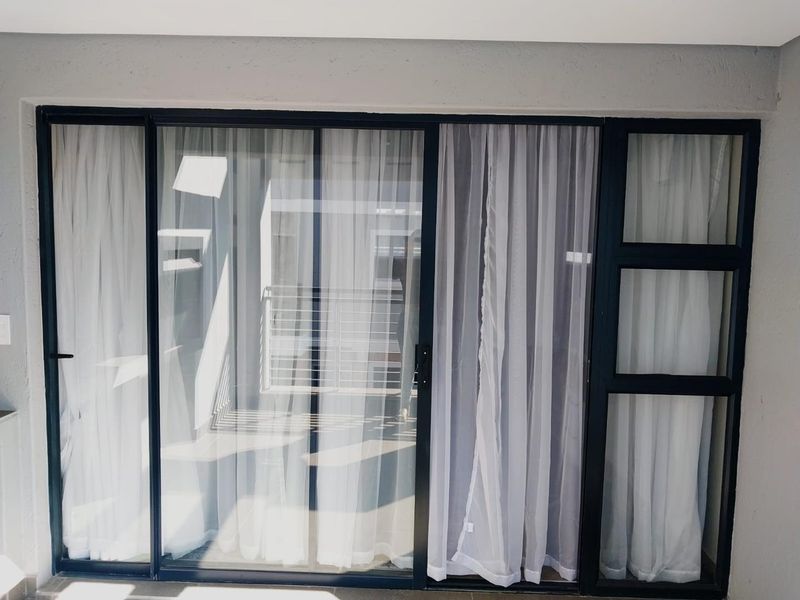 A view of a modern apartment balcony featuring black aluminum sliding glass doors and fixed window panels.