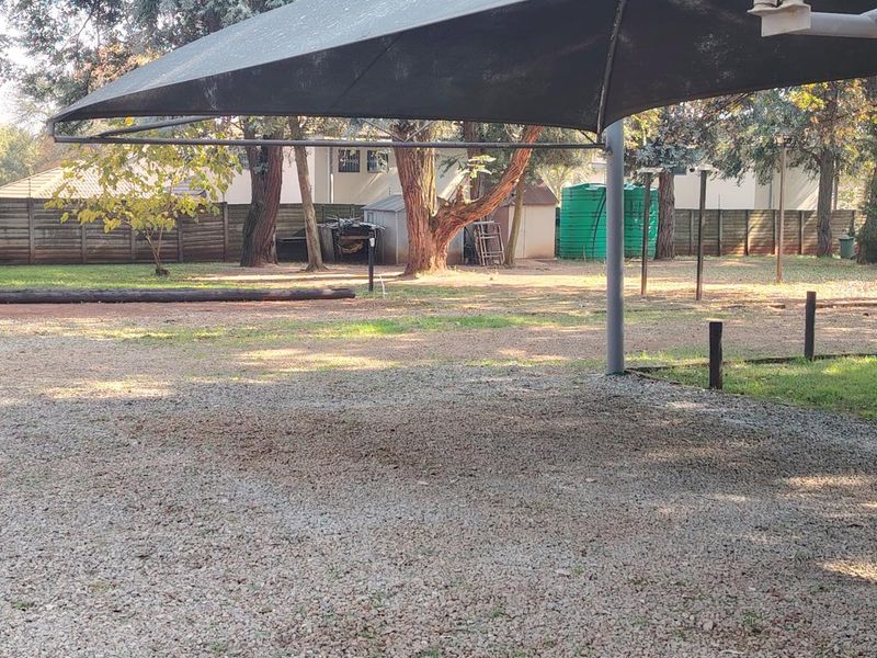 A spacious outdoor area featuring a gravel driveway, a large shade sail structure, and a water storage tank set within a fenced garden.