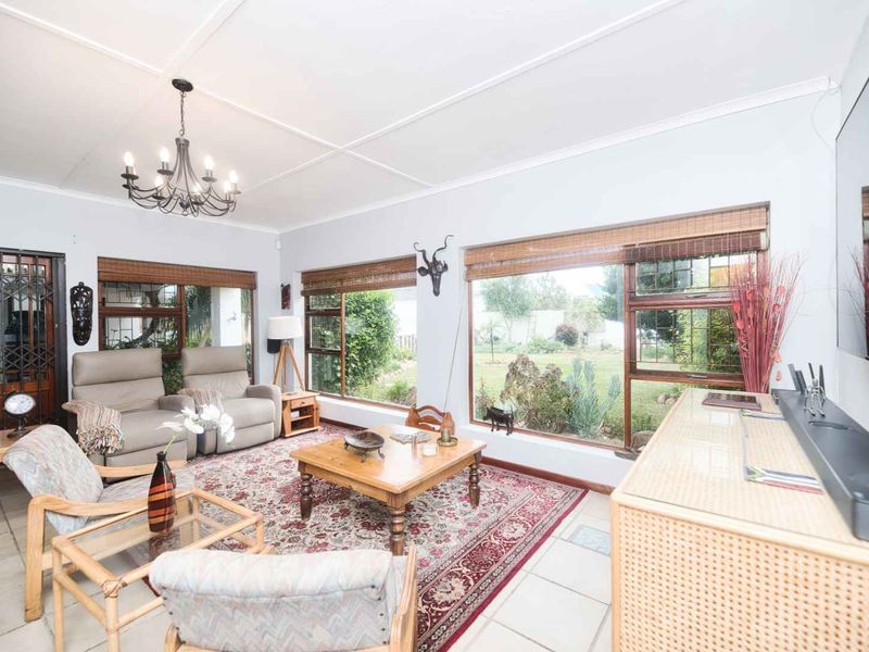A bright living room featuring tiled flooring, large windows overlooking the garden, and a security gate at the entrance.