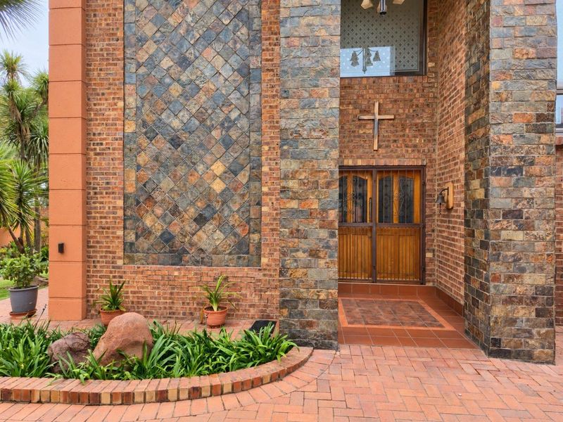 Front entrance featuring a distinctive slate tile facade, face brick construction, and a paved driveway with a raised garden bed.