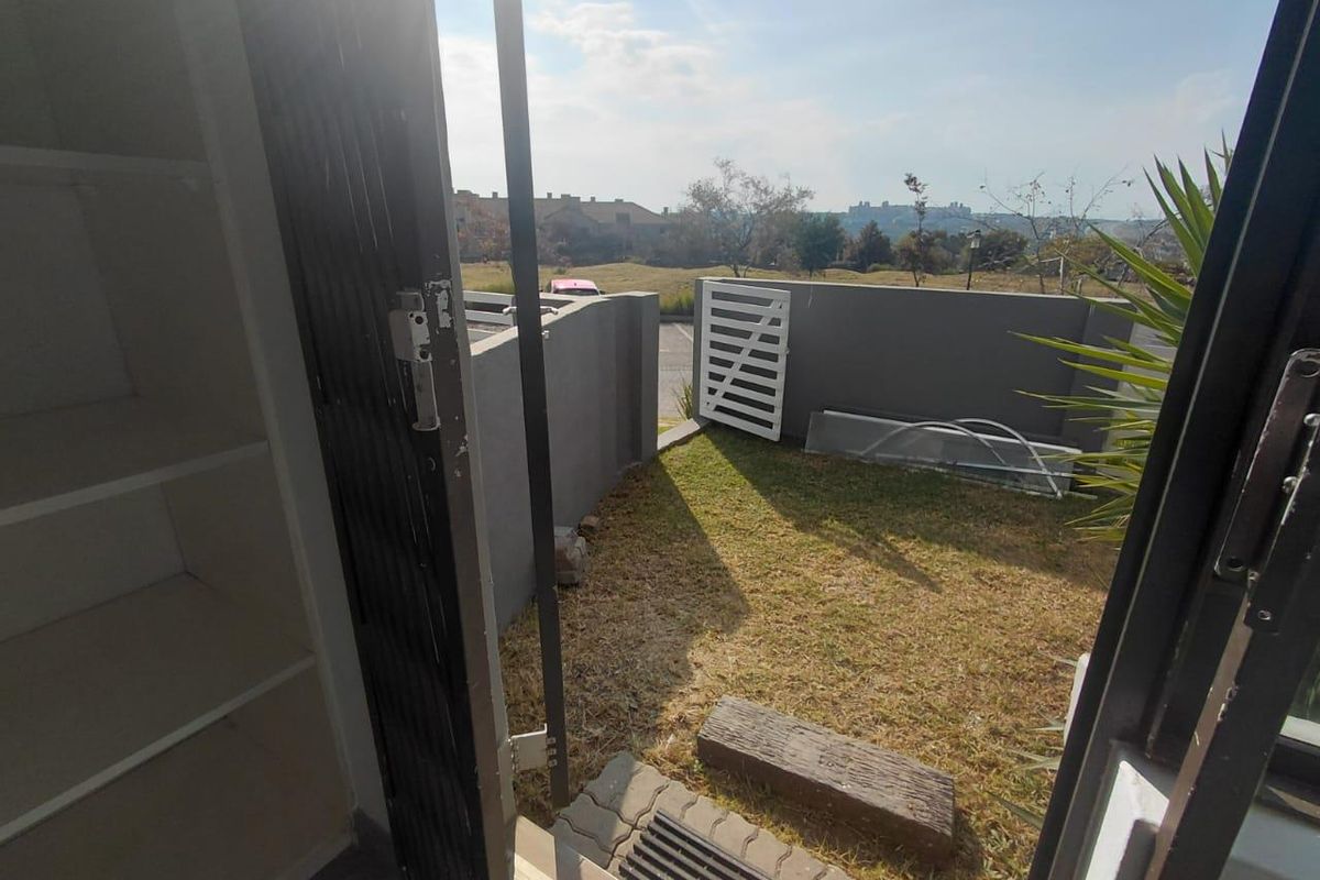 A small private rear garden area featuring a paved walkway, boundary wall, and security gate access, offering potential for outdoor landscaping.