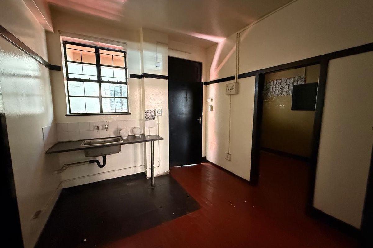 A basic, empty kitchen area featuring a stainless steel sink, tiled splashback, and painted concrete flooring, requiring significant cosmetic updates.