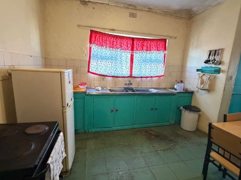 A dated kitchen featuring original cabinetry, tiled flooring, and a stainless steel sink, requiring significant renovation and cosmetic updates to modernize the space.