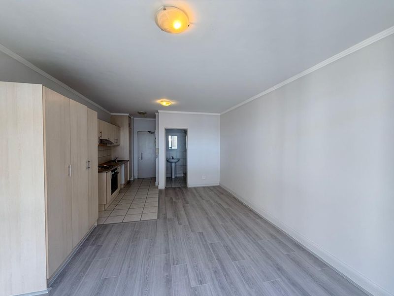 An open-plan living area featuring a compact kitchen with built-in cabinetry, integrated oven, and extractor fan, leading to a separate bathroom area.