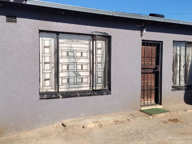 Front elevation of a single-story house featuring a textured grey facade, security gates, and metal window bars.