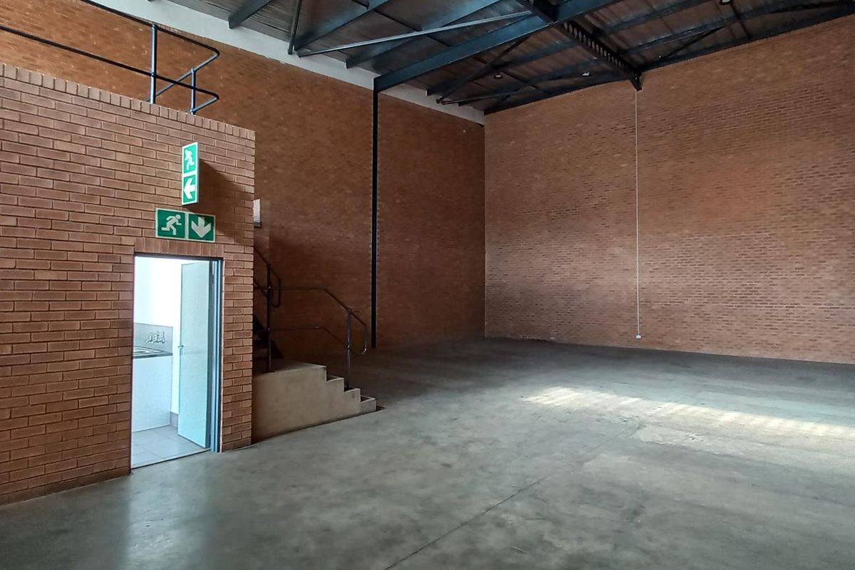 Spacious industrial warehouse unit featuring high ceilings with exposed steel trusses, durable concrete flooring, and brick wall finishes with a mezzanine access point.