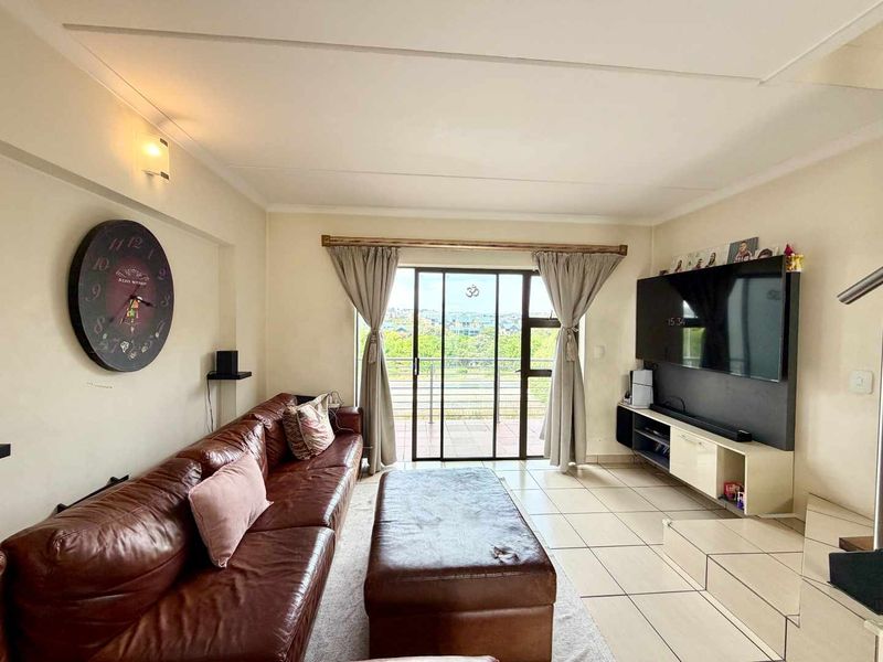 A comfortable living room featuring tiled flooring and a sliding glass door that provides access to an outdoor balcony with scenic views.