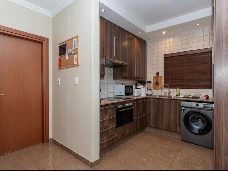 Compact kitchen featuring modern wood-finish cabinetry, tiled backsplash, built-in oven with hob, and integrated space for a washing machine.
