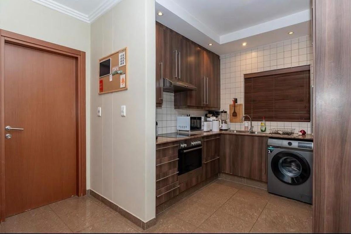 Compact kitchen featuring modern wood-finish cabinetry, tiled backsplash, built-in oven with hob, and integrated space for a washing machine.