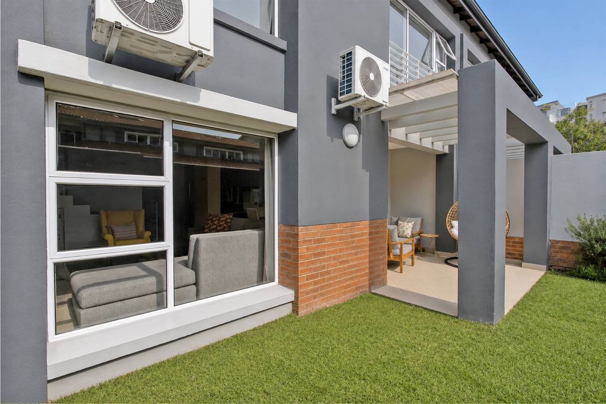 Rear view of the townhouse featuring a covered patio area, manicured lawn, and exterior wall-mounted air conditioning units.