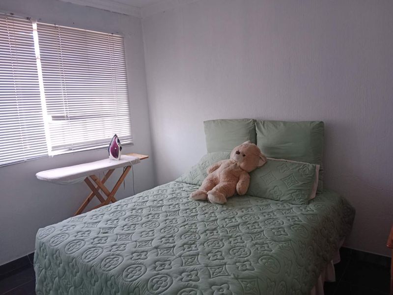 A simple bedroom featuring tiled flooring, white walls, and venetian blinds, providing a functional and neutral space.