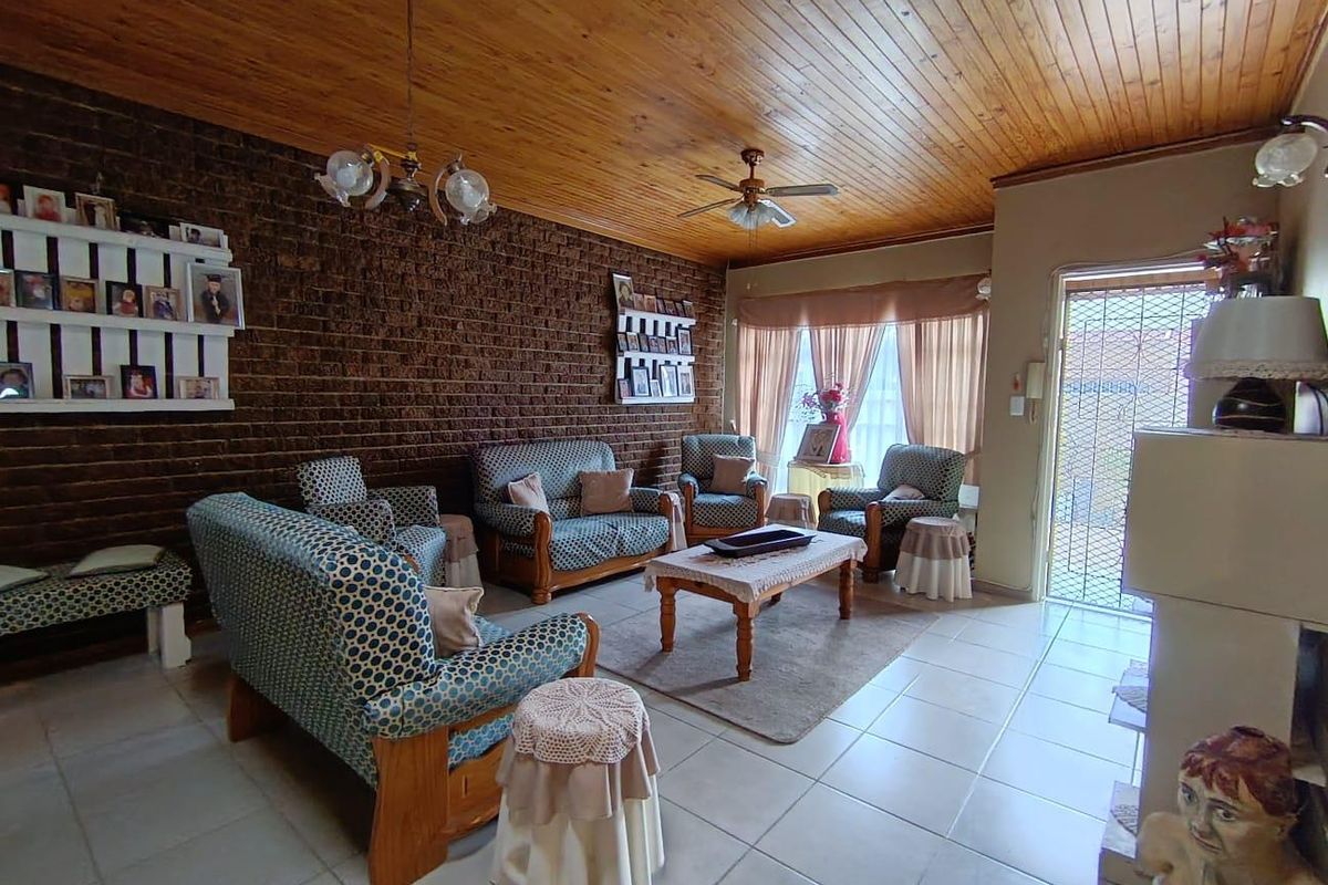 A spacious living room featuring a prominent exposed brick feature wall, tiled flooring, and a timber-clad ceiling with a central ceiling fan.