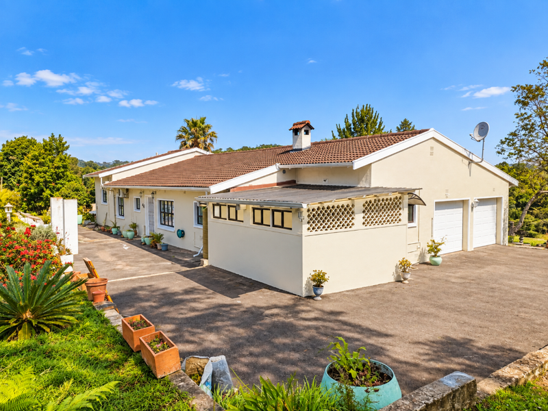 A well-maintained single-story house featuring a tiled roof, double garage, and a paved driveway with a covered patio area.