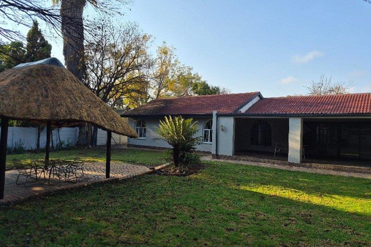 Rear garden featuring a paved patio area with a traditional thatched lapa, lawn, and a covered veranda attached to the main house structure.