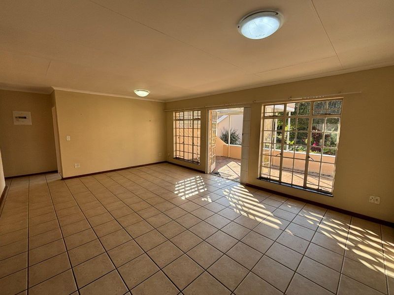 Spacious, sunlit living area featuring neutral tiled flooring and large grid-pattern windows with direct access to an outdoor patio space.