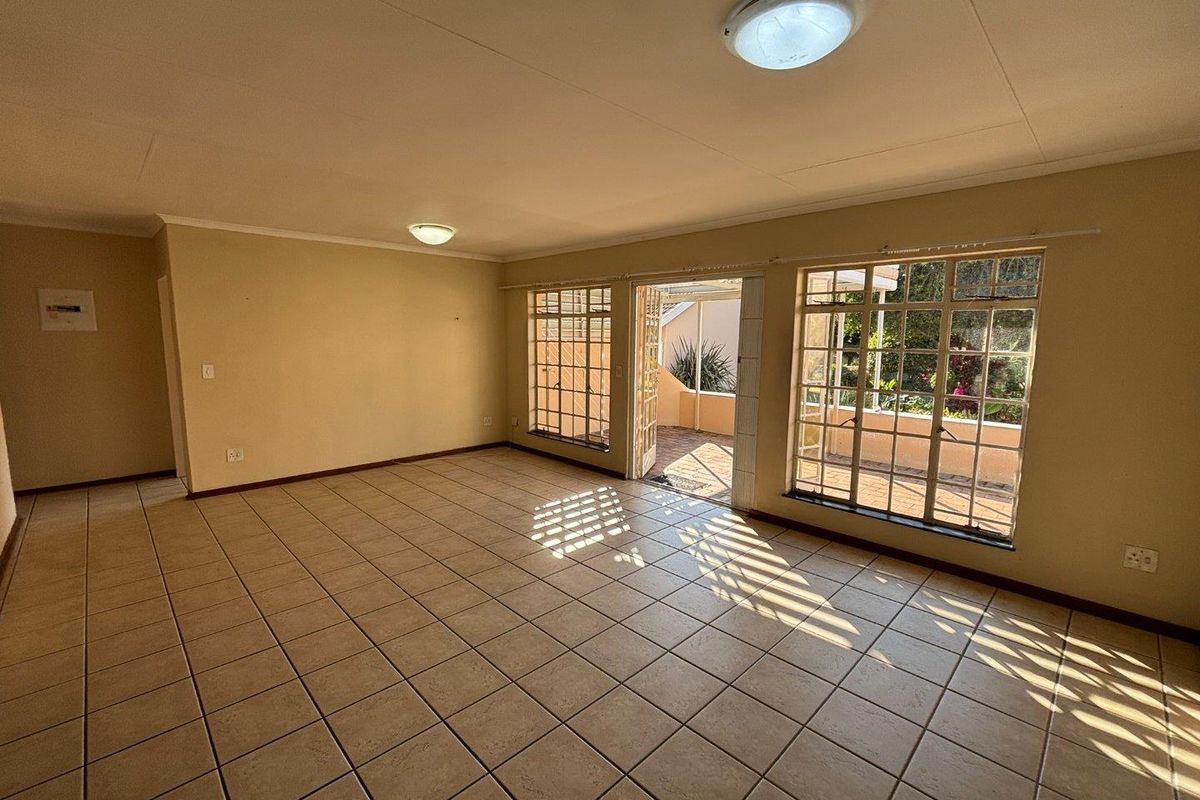 Spacious, sunlit living area featuring neutral tiled flooring and large grid-pattern windows with direct access to an outdoor patio space.