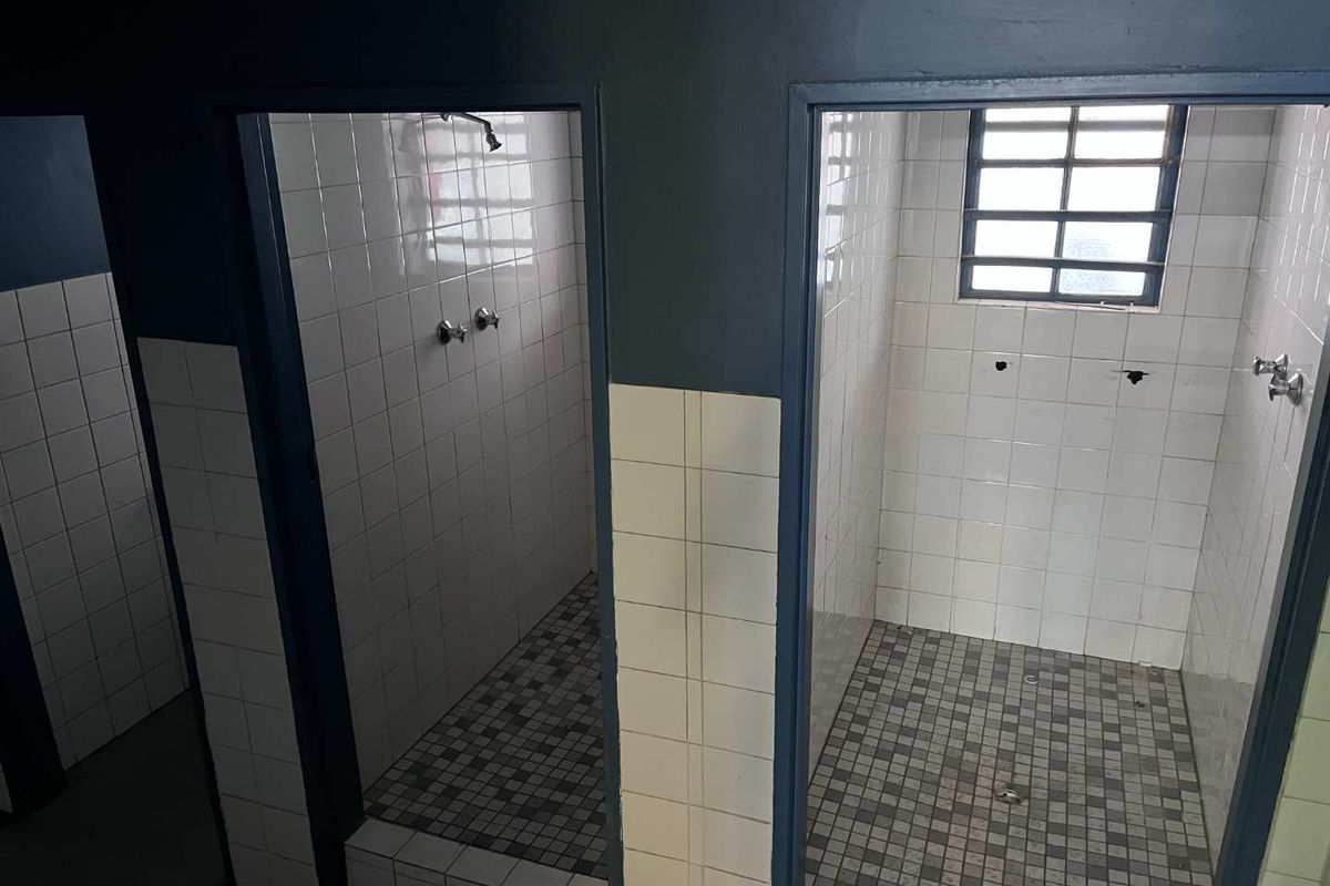 Industrial-style communal shower facility featuring tiled walls, mosaic floor tiles, and multiple shower cubicles with exposed plumbing fixtures.