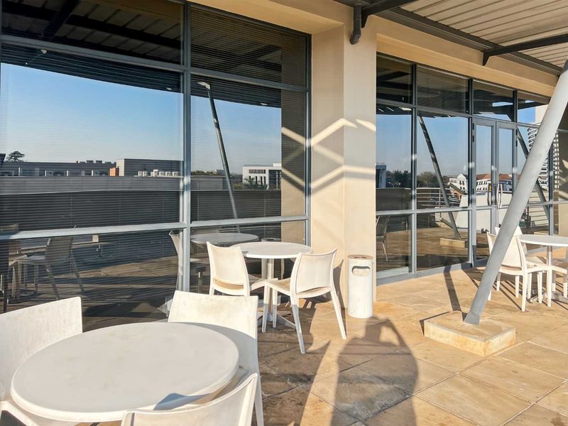A spacious outdoor balcony area featuring large glass office windows, tiled flooring, and structural metal supports, providing a functional exterior space for the office building.