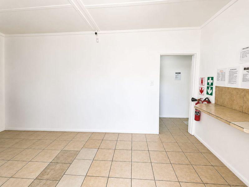 A clean, empty utility space featuring tiled flooring, a fixed counter, and safety equipment including a fire extinguisher and security camera.