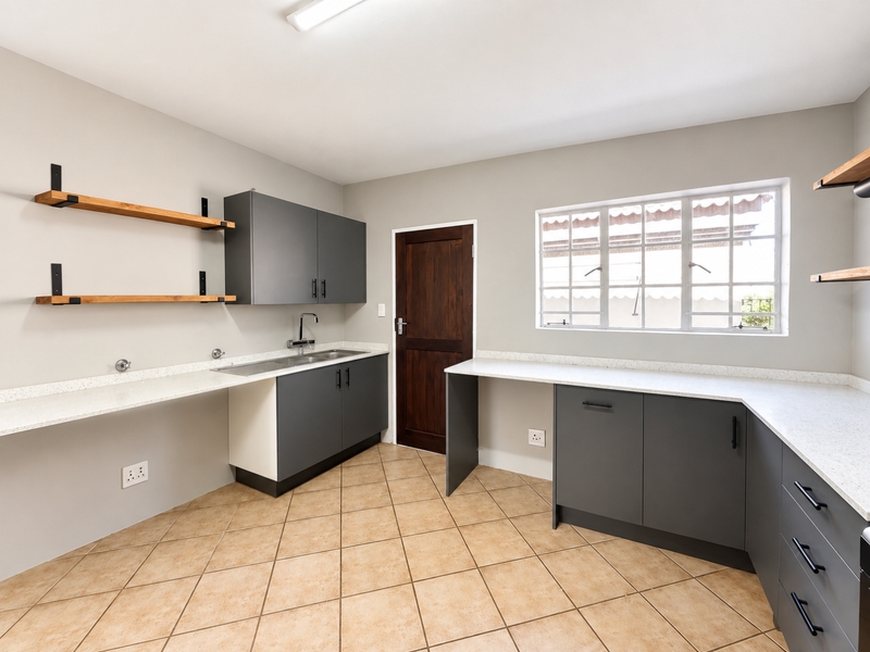 A clean and modern laundry room featuring grey cabinetry, stone countertops, a stainless steel sink, and tiled flooring with ample storage space.