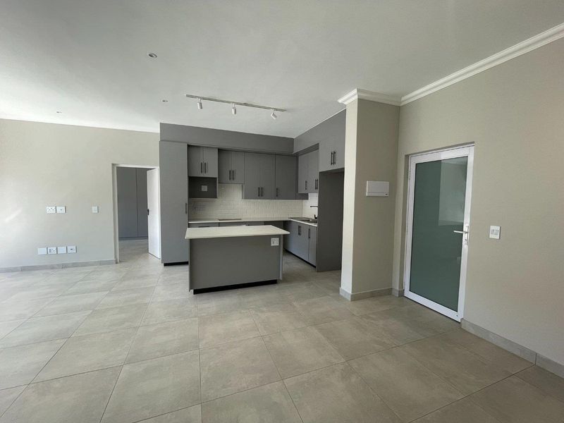Modern open-plan kitchen featuring grey cabinetry, a central island, subway tile backsplash, and neutral tiled flooring in a bright, spacious living area.