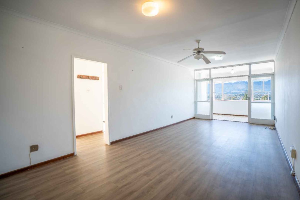 A bright, empty living room featuring laminate flooring, a ceiling fan, and direct access to a balcony with scenic mountain views.