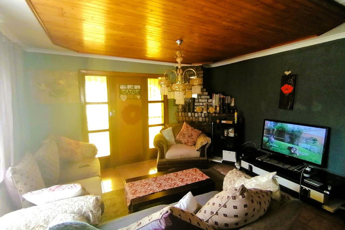 A cozy living room featuring a brick fireplace, wooden tongue-and-groove ceiling, and tiled flooring, providing a warm and traditional atmosphere.