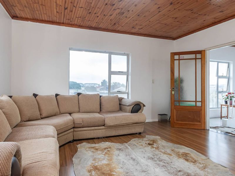 A living room featuring a timber-clad ceiling, laminate flooring, and a classic timber-framed glass door leading to an adjacent space.
