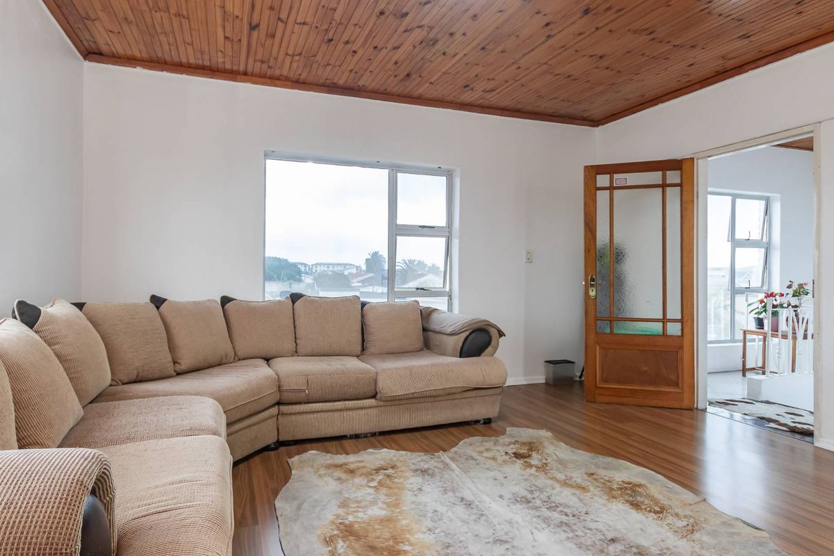 A living room featuring a timber-clad ceiling, laminate flooring, and a classic timber-framed glass door leading to an adjacent space.