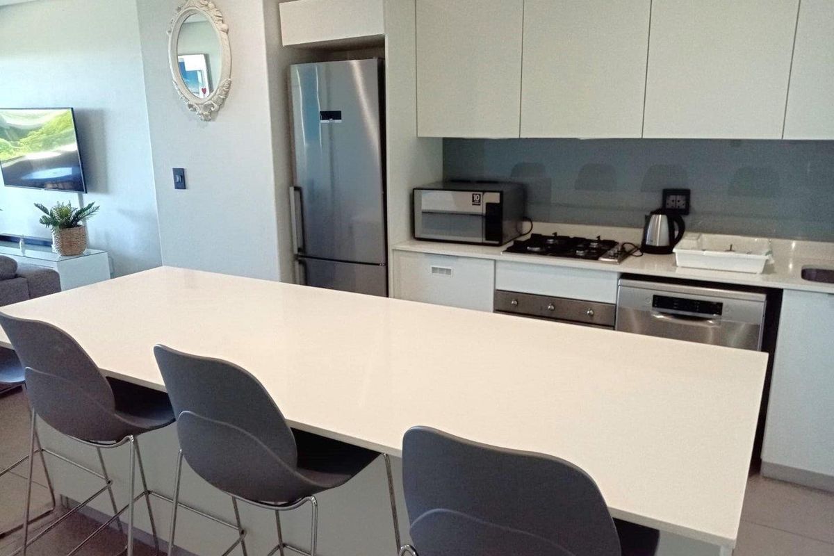 Modern kitchen featuring a large quartz breakfast island, handleless white cabinetry, integrated dishwasher, gas hob, and stainless steel appliances.