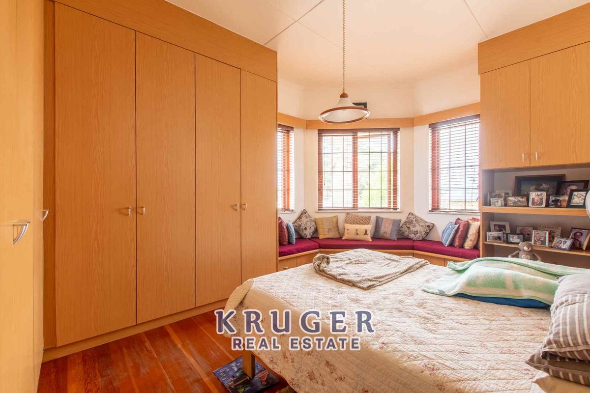 Bedroom featuring extensive built-in wooden cabinetry, a bay window with a built-in bench seat, and timber flooring.