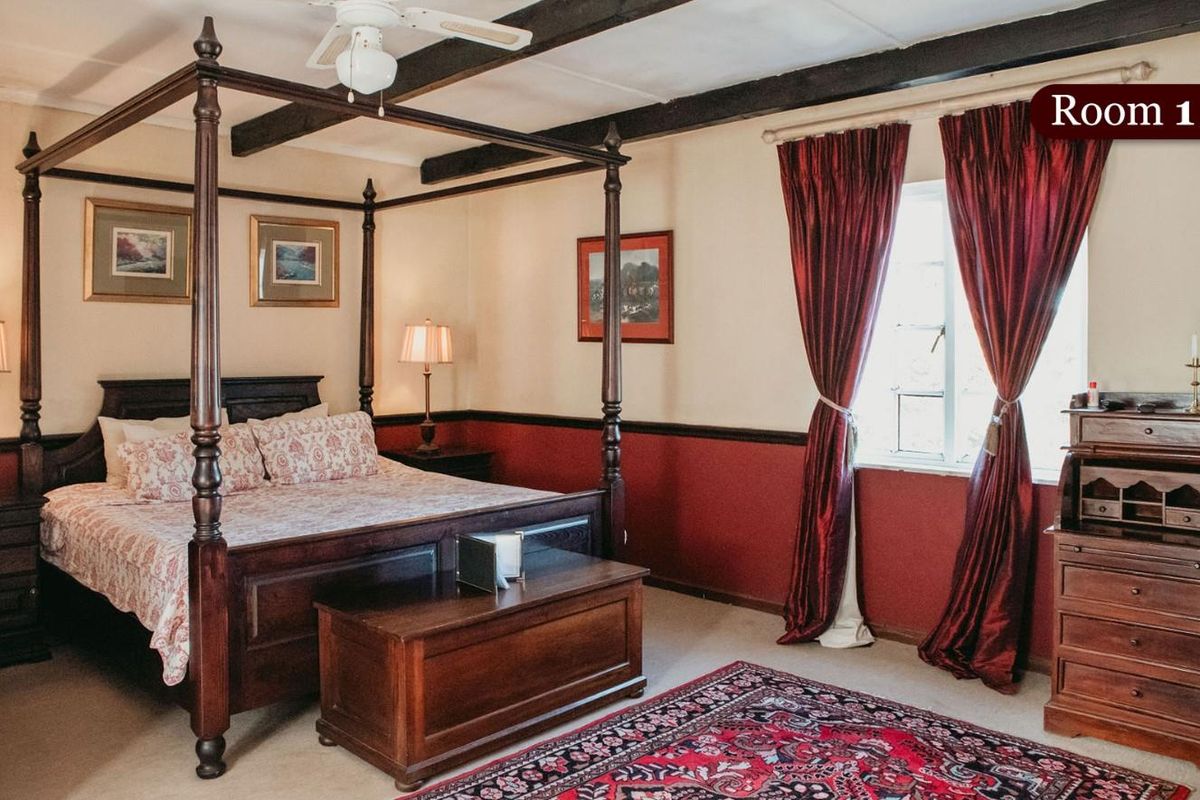 A spacious bedroom featuring exposed timber ceiling beams, a four-poster bed frame, and traditional wall paneling with a classic color scheme.