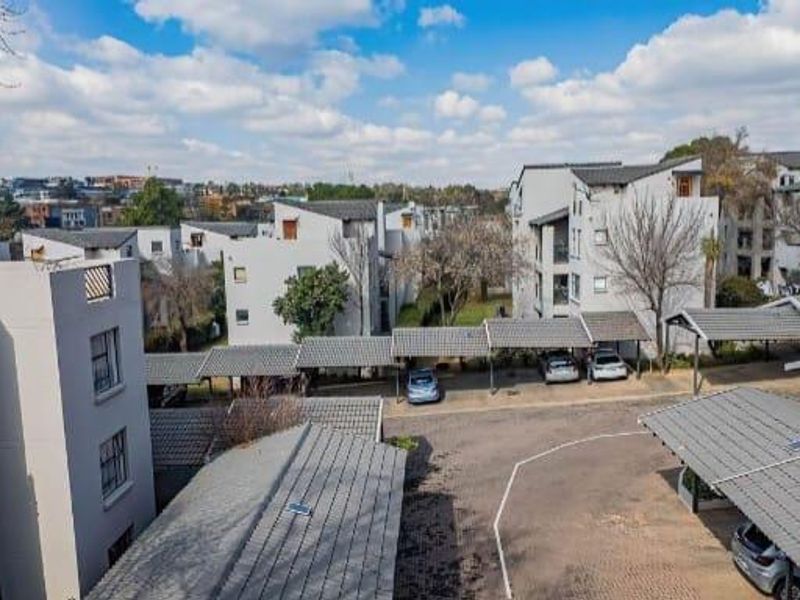 An elevated aerial view of the apartment complex, showcasing the residential buildings, paved driveway, and covered parking bays.