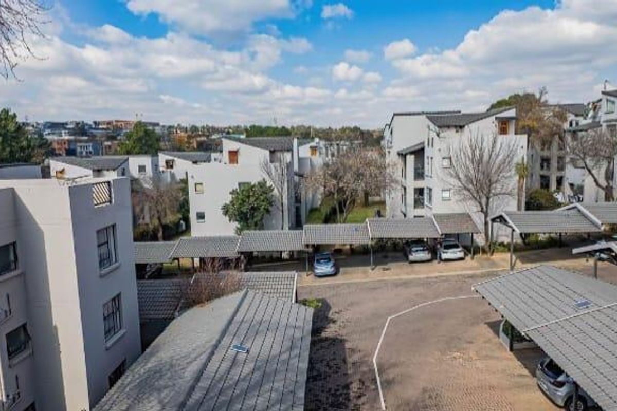 An elevated aerial view of the apartment complex, showcasing the residential buildings, paved driveway, and covered parking bays.