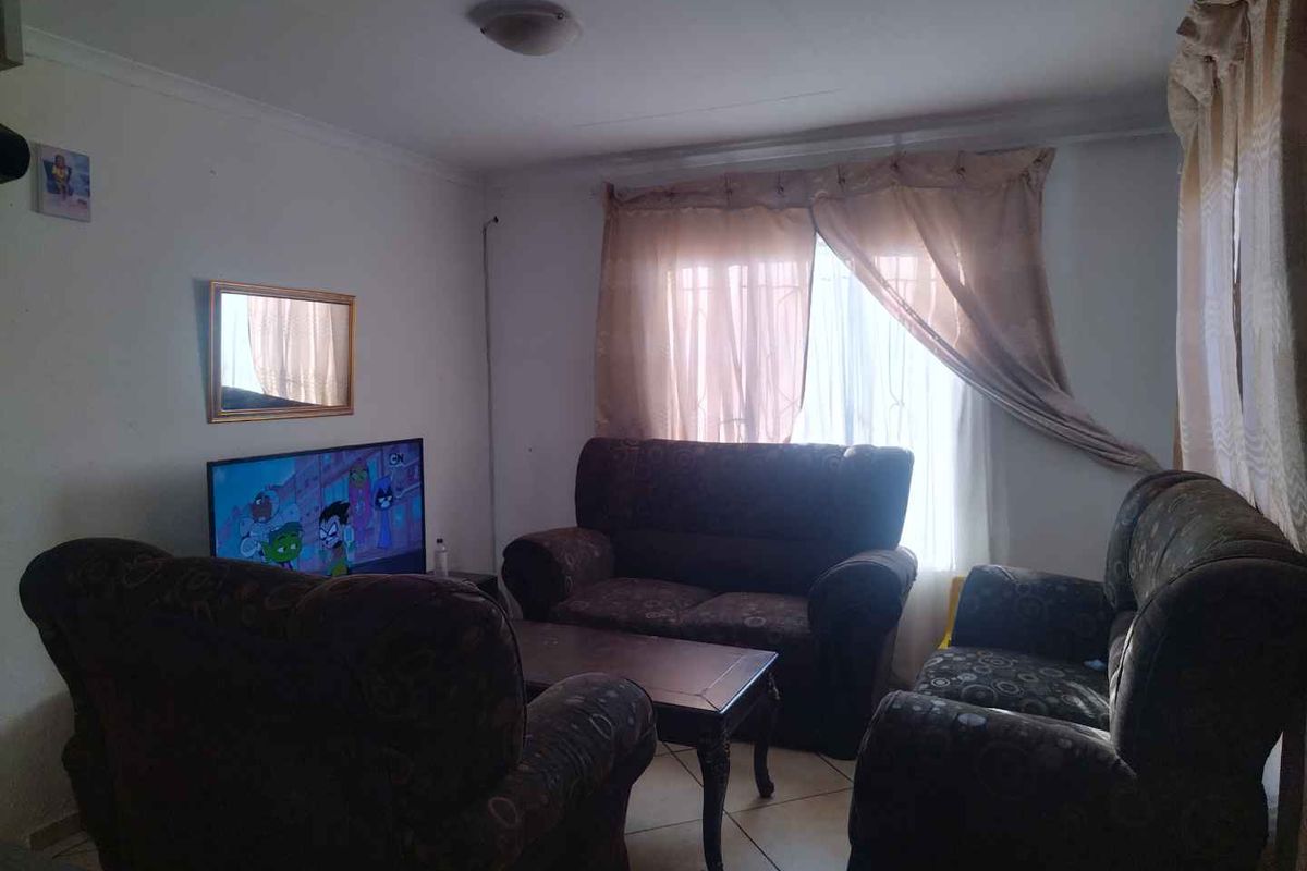 A functional living room featuring tiled flooring and large windows with curtains, providing a comfortable space for relaxation.
