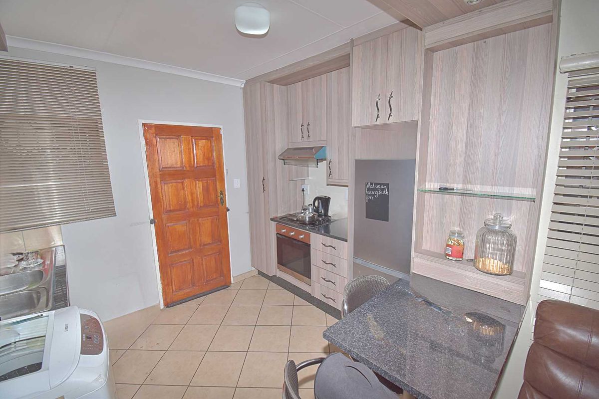 Compact kitchen featuring wood-look cabinetry, built-in oven and hob, granite-topped breakfast bar, and tiled flooring with direct access to an exterior door.