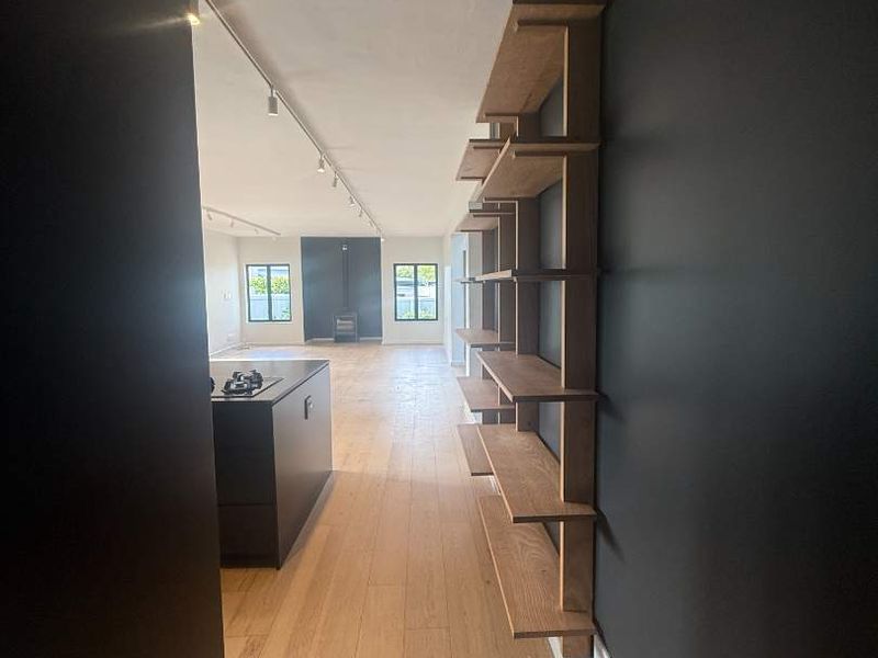Spacious open-plan living area featuring timber flooring, modern track lighting, built-in wall shelving, and a central kitchen island with a wood-burning stove.